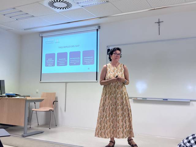 Una mujer está de pie frente a una pantalla de proyección dando una presentación en un aula.