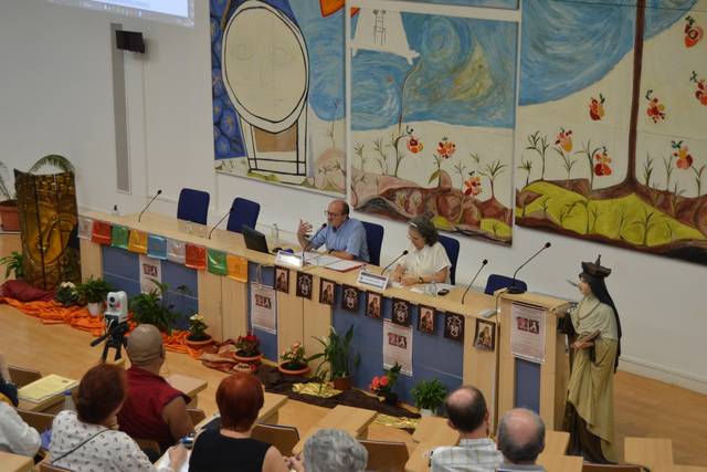 A panel discussion in a conference room with colorful paintings and a small audience.