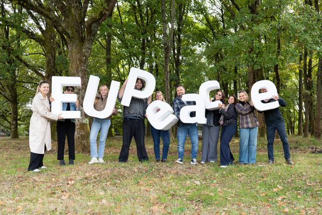 Un grupo de personas sosteniendo letras que forman la palabra 'EU Peace' en un entorno natural.