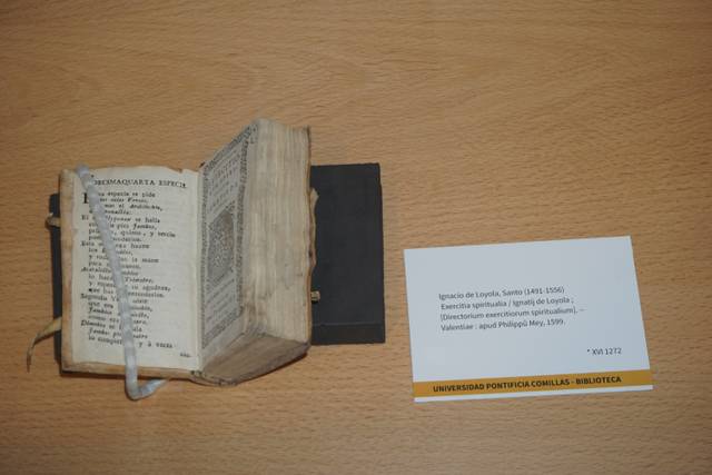 Un libro antiguo abierto con una hoja suelta al lado que contiene información sobre su autor y su ubicación.