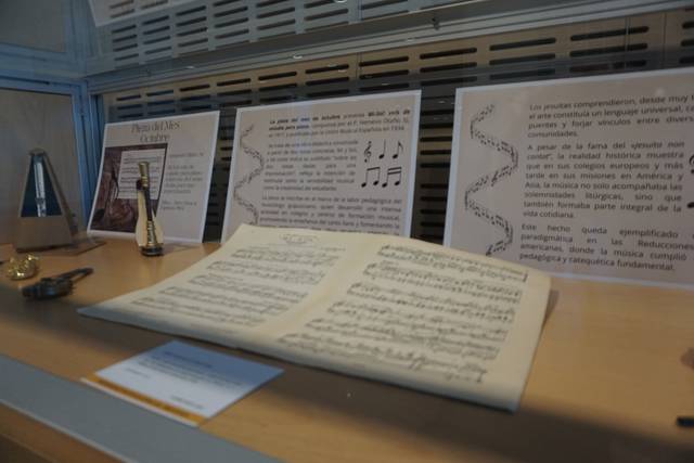 La imagen muestra una exposición sobre música, con partituras, textos explicativos y otros objetos relacionados.