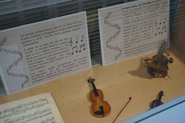 La imagen muestra un exhibidor con partituras, instrumentos musicales como violines y textos informativos sobre la música y compositores.
