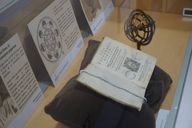 La imagen muestra un libro antiguo sobre un cojín, acompañado de un globo terráqueo y una serie de documentos en el fondo.