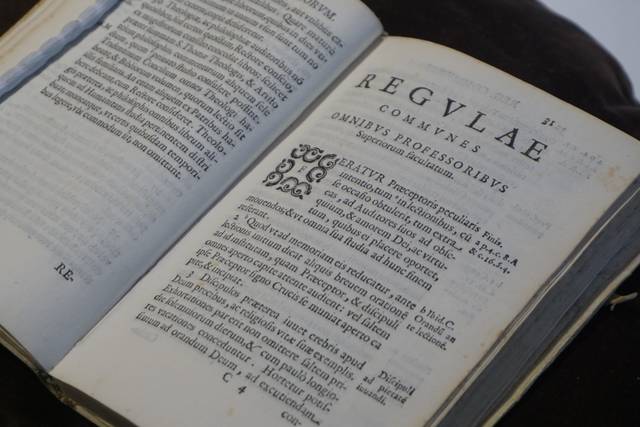 Un libro antiguo abierto que muestra texto impreso en latín y un diseño ornamentado en la página.