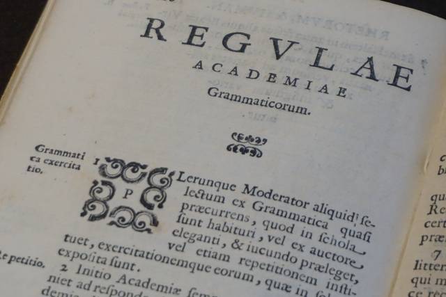 La imagen muestra una página de un libro antiguo con títulos y texto en latín relacionados con gramática.