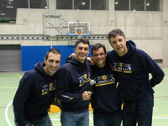 Four men smiling in a sports hall, wearing matching blue hoodies labeled 'Comillas'.