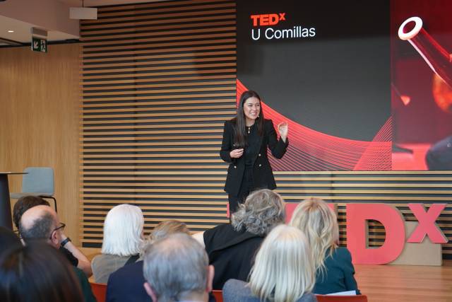 Una oradora presenta en un evento TEDx en un ambiente moderno y acogedor.