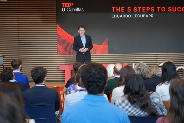 Un conferencista presenta en un evento TEDx en U Comillas, mientras el público escucha atentamente.