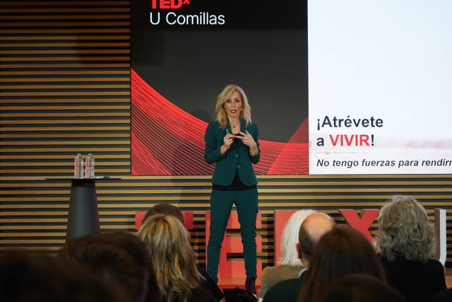 Una mujer de pie en un escenario durante una charla TED, animando al público a atreverse a vivir.