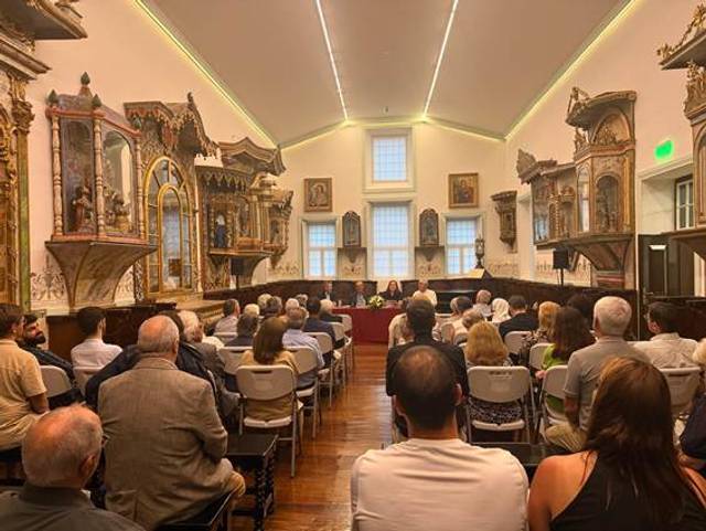La imagen muestra a un grupo de personas en una sala con decoraciones artísticas y una presentación en curso.