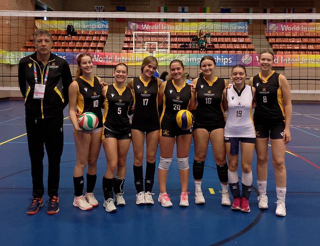 El equipo de voleibol femenino posando en la cancha con pelotas de voleibol y un entrenador.