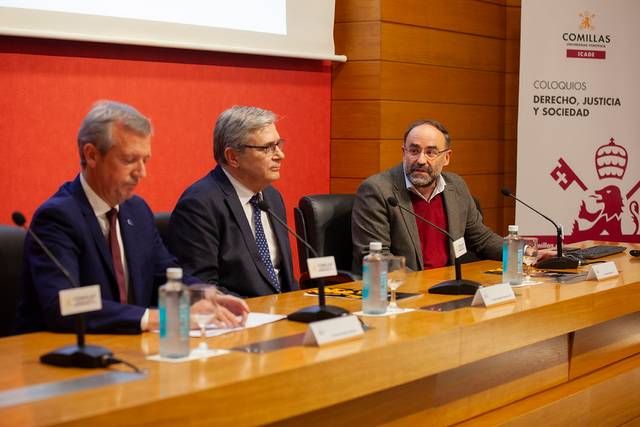 Three men sitting at a panel discussion table in a conference room.