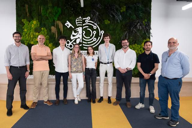 Un grupo de personas está posando en un entorno moderno con decoración vegetal de fondo.