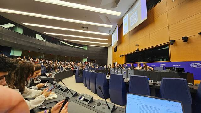 Una sala de conferencias llena de gente, con varias personas utilizando teléfonos móviles y pantallas en el fondo.