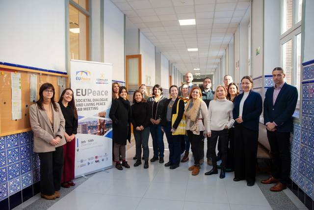 Un grupo de personas posa para una foto en un pasillo de edificio con decoración de azulejos azules.