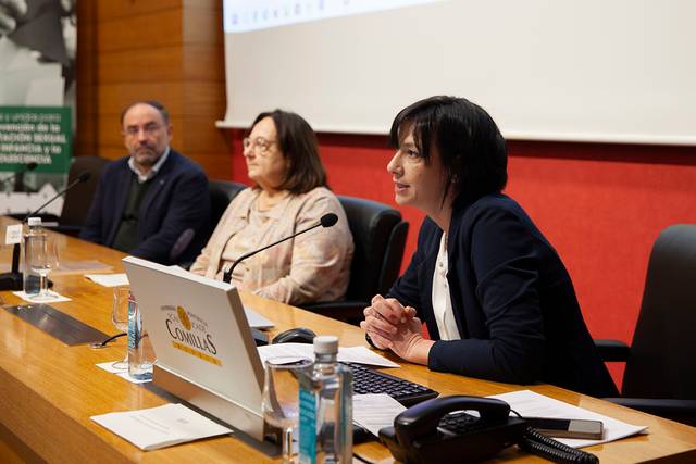 Una mujer habla en un micrófono durante una conferencia con otros dos participantes sentados a su lado.