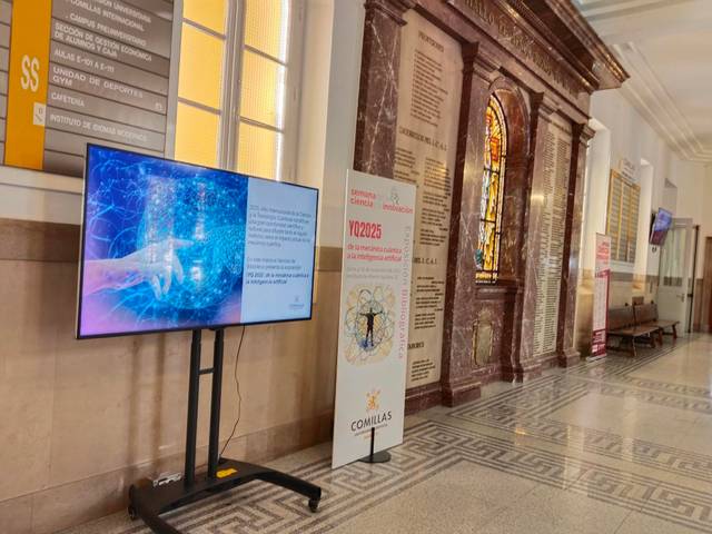 Una pantalla digital muestra una presentación interactiva en un pasillo con vitrales y decoración arquitectónica.