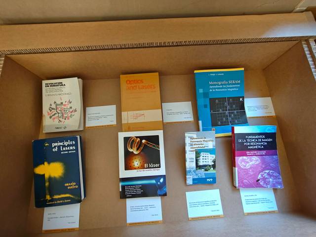 Una caja de cartón que contiene varios libros sobre óptica y láseres dispuestos ordenadamente.
