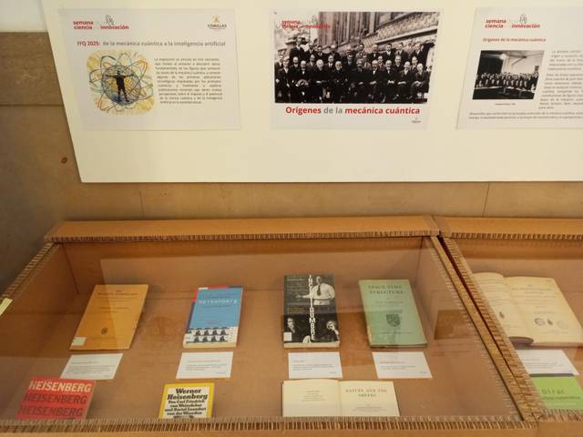 La imagen muestra una vitrina con libros y documentos relacionados con la mecánica cuántica y la inteligencia artificial.