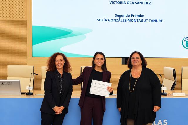 Una joven recibe un premio mientras sonríe, acompañada por dos mujeres en un evento de entrega de galardones.