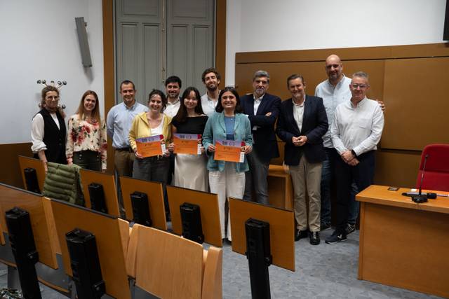 Un grupo de personas sonríe sosteniendo diplomas en un aula.