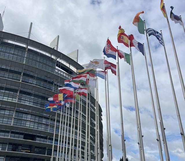 Edificio moderno con banderas de diferentes países ondeando frente a él.