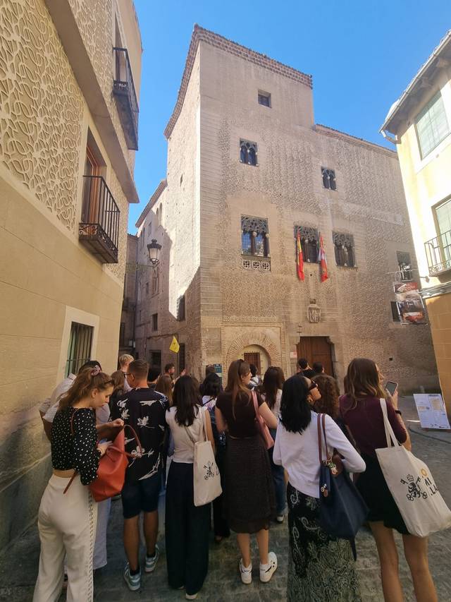 Un grupo de personas observa un edificio histórico en una calle estrecha y soleada.