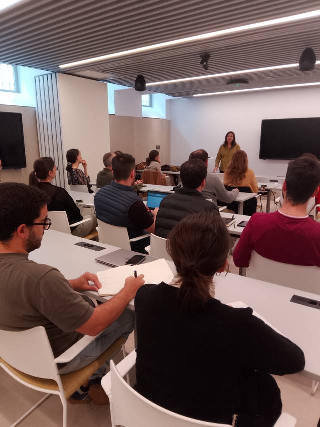 Una presentación se lleva a cabo en un aula moderna con varias personas sentadas escuchando.