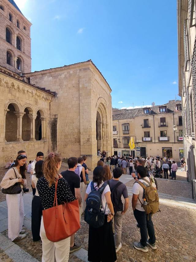 Una multitud de personas se agrupa en una plaza cerca de un edificio histórico y soleado.