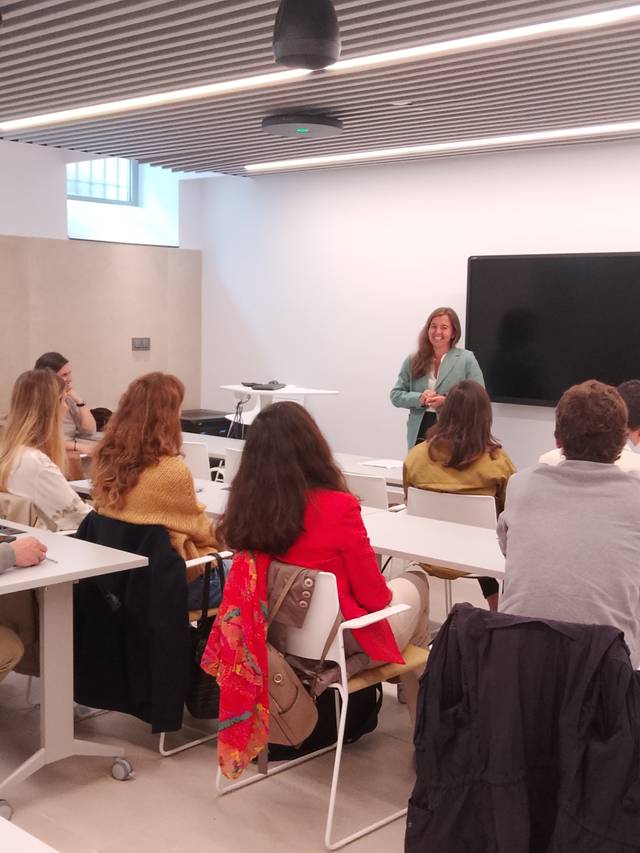 Una mujer está dando una presentación frente a un grupo de personas en un salón moderno.