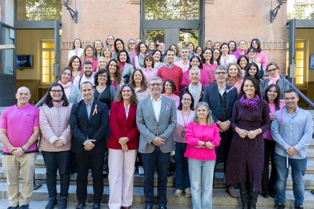 Un grupo grande de personas vestido de rosa posa en la entrada de un edificio.