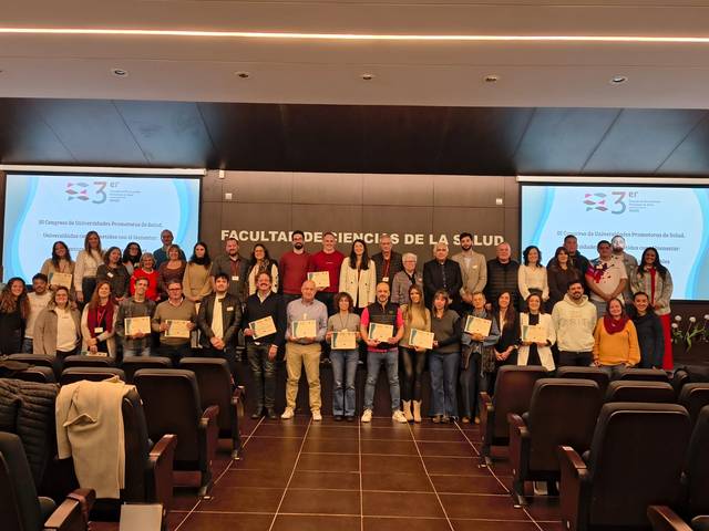 Un grupo de personas se encuentra en un auditorio, sosteniendo certificados de un evento académico.