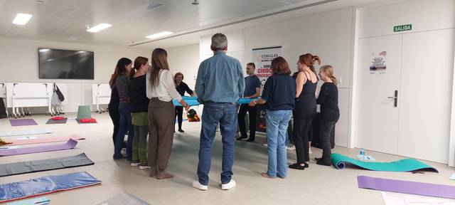 Un grupo de personas se encuentra en un salón, sosteniendo una larga tela mientras participan en una actividad grupal.