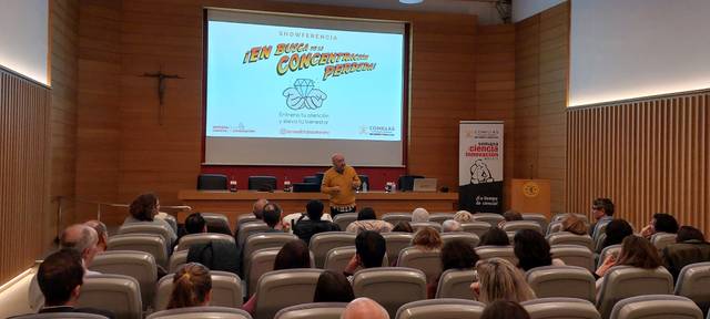 Una conferencia con un ponente en un escenario frente a una audiencia en un auditorio.