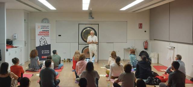 Un grupo de personas se encuentra sentado en el suelo, escuchando a un ponente en un evento sobre ciencia e innovación.