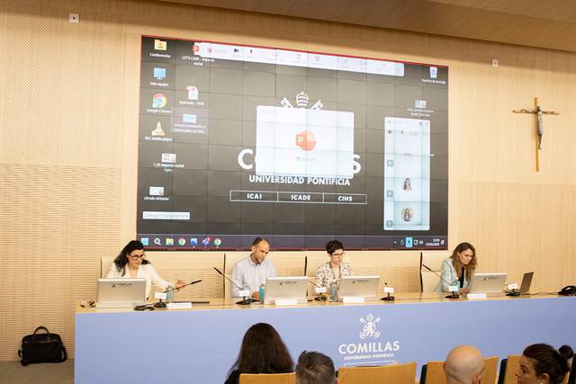 Una mesa de conferencias en la Universidad Pontificia Comillas con presentadores y una pantalla grande detrás.