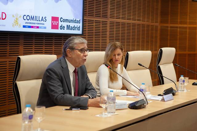 Un acto en el que dos personas se encuentran en una mesa de conferencias con agua y material de exposición.