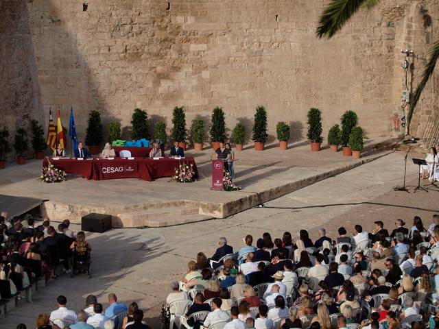 Una ceremonia al aire libre con un escenario y una gran audiencia sentada.