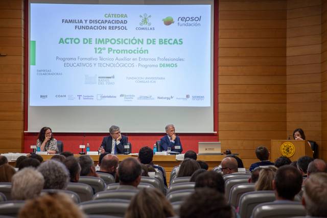 Un evento formal de imposición de becas en una sala con un público atento y ponentes en el escenario.