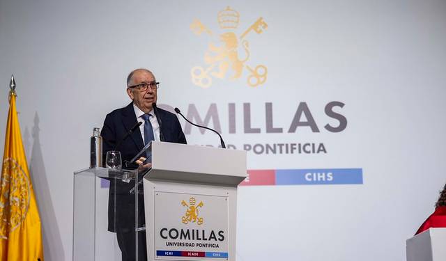 Un hombre mayor está dando un discurso en un podio con el logo de la Universidad Pontificia Comillas de fondo.
