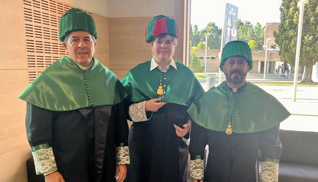 Tres personas vestidas con trajes académicos tradicionales se posan juntas en un ambiente formal.
