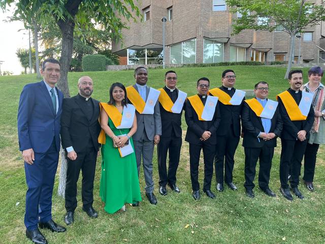 Un grupo de graduados posando con togas y birretes en una ceremonia al aire libre.