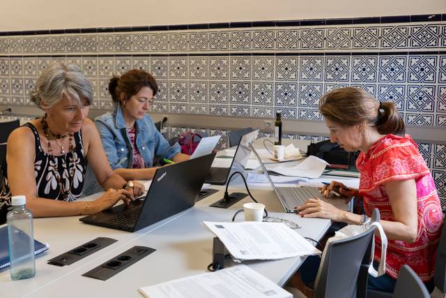 Tres mujeres trabajando en un entorno colaborativo con computadoras portátiles y documentos sobre la mesa.