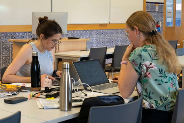 Dos estudiantes trabajan en una mesa, concentradas en sus computadoras portátiles.