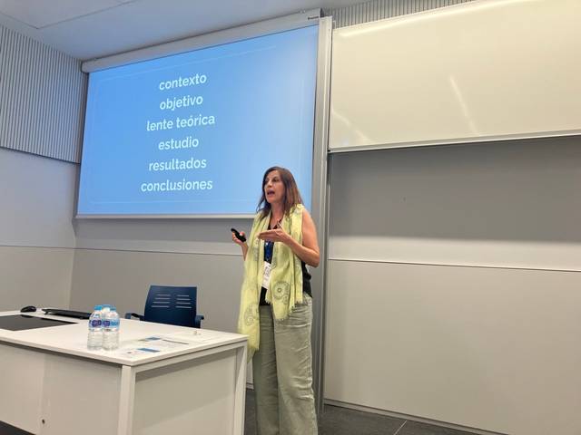 Una mujer presenta información en una sala de conferencias sobre un tema académico.