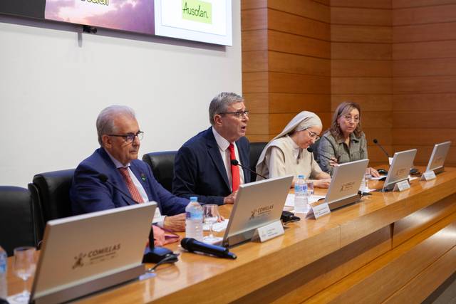 Una mesa de debate con cuatro personas sentadas, incluyendo un hombre de gafas y una mujer con hábito religioso.