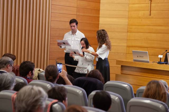 Tres personas participan en una presentación frente a una audiencia en un ambiente académico.