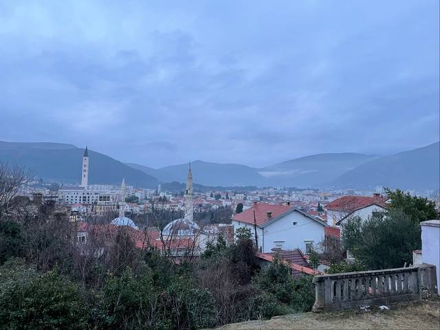 Vista panorámica de una ciudad rodeada de montañas bajo un cielo nublado.