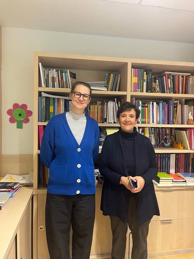 Dos mujeres sonríen frente a una estantería llena de libros en un ambiente acogedor.