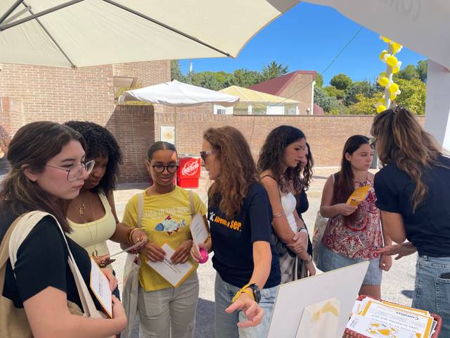 Un grupo de jóvenes interactúa en un evento al aire libre bajo una sombrilla.